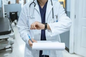 A male doctor in a white coat holding a clipboard