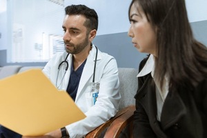 A Doctor and person sitting in chairs looking at a file